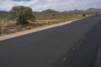 a long empty road in a desert landscape is seen from the passenger seat of a vehicle