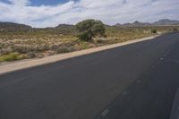 a long empty road in a desert landscape is seen from the passenger seat of a vehicle