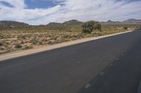 a long empty road in a desert landscape is seen from the passenger seat of a vehicle