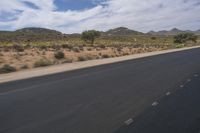 a long empty road in a desert landscape is seen from the passenger seat of a vehicle