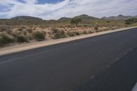 a long empty road in a desert landscape is seen from the passenger seat of a vehicle