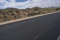 a long empty road in a desert landscape is seen from the passenger seat of a vehicle