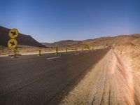 several signs are positioned on the side of a road by a fence in the desert