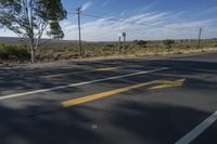 a road with yellow stripe in an open area next to a telephone pole with wires in it