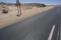 a red sign with white lines is on a desert road in the afternoon sun and blue sky