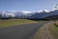 a long stretch of road with grass and mountains in the background with dark clouds above