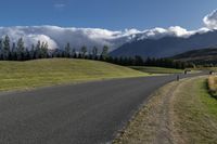 a long stretch of road with grass and mountains in the background with dark clouds above