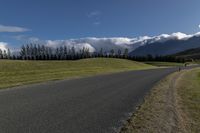 a long stretch of road with grass and mountains in the background with dark clouds above