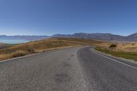 an empty road with the view of some mountains and water in the background with a blue sky