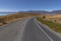 an empty road with the view of some mountains and water in the background with a blue sky