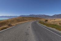 an empty road with the view of some mountains and water in the background with a blue sky