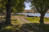 two boats parked on a field near a river and trees in front of it in the sunlight