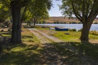 two boats parked on a field near a river and trees in front of it in the sunlight