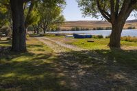 two boats parked on a field near a river and trees in front of it in the sunlight