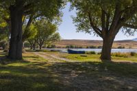 two boats parked on a field near a river and trees in front of it in the sunlight