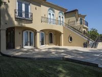 a large house with some stairs and lawn in front of it, with a grill and two patio areas next to it