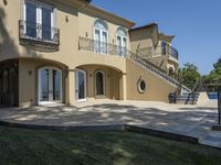 a large house with some stairs and lawn in front of it, with a grill and two patio areas next to it