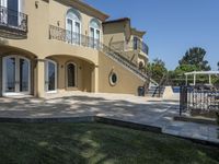 a large house with some stairs and lawn in front of it, with a grill and two patio areas next to it