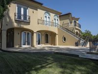 a large house with some stairs and lawn in front of it, with a grill and two patio areas next to it