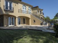 a large house with some stairs and lawn in front of it, with a grill and two patio areas next to it