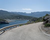 the road has been curved with no side railings along it near a body of water and a small yacht harbor