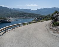 the road has been curved with no side railings along it near a body of water and a small yacht harbor