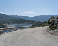 the road has been curved with no side railings along it near a body of water and a small yacht harbor