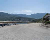 the road has been curved with no side railings along it near a body of water and a small yacht harbor