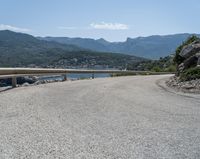 the road has been curved with no side railings along it near a body of water and a small yacht harbor