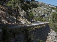 a road with a long curve through the mountains, with trees and a rock wall beside it