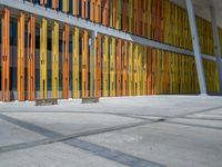 a concrete structure made into rows of orange and yellow poles are on a cement sidewalk