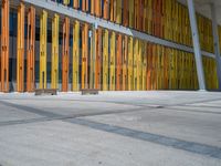 a concrete structure made into rows of orange and yellow poles are on a cement sidewalk