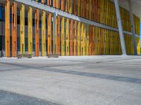 a concrete structure made into rows of orange and yellow poles are on a cement sidewalk