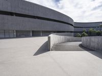 concrete surface with curved walls on a large building's outside space that is surrounded by large, low trees