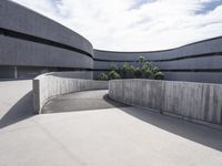 concrete surface with curved walls on a large building's outside space that is surrounded by large, low trees