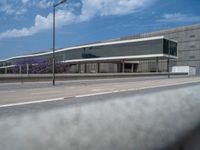 a car driving on the road near an empty parking lot and warehouse building that has white railings