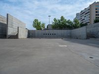 the empty parking lot in front of a wall with apartment buildings on it and a skateboarder on a ramp