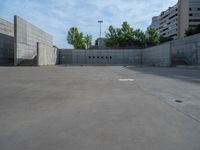 the empty parking lot in front of a wall with apartment buildings on it and a skateboarder on a ramp