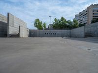 the empty parking lot in front of a wall with apartment buildings on it and a skateboarder on a ramp