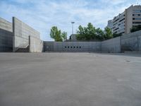 the empty parking lot in front of a wall with apartment buildings on it and a skateboarder on a ramp