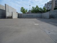 the empty parking lot in front of a wall with apartment buildings on it and a skateboarder on a ramp