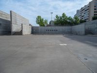 the empty parking lot in front of a wall with apartment buildings on it and a skateboarder on a ramp