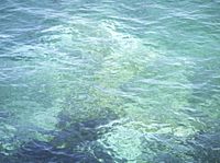 a blue ocean has a boat in the water and waves are moving around it in this photo