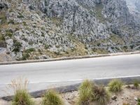 the motorcycle is traveling on the street near a mountain wall side road and mountains below