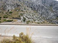 the motorcycle is traveling on the street near a mountain wall side road and mountains below