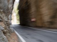 a blurry image of a tunnel on the road by a stone wall and sign