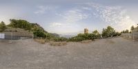 a very wide lens shot of a hill overlooking a river and mountains on a bright, summer day