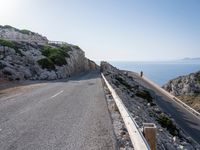 a cyclist is riding on a steep hill road overlooking the ocean and some rocks,