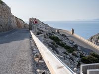 a cyclist is riding on a steep hill road overlooking the ocean and some rocks,