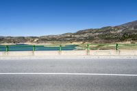 this is the empty road in front of the water and hills, along side the road, that leads to a small parking area